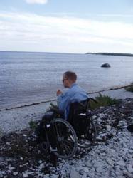 Hkan Pettersson sitter i en rullstol p en stenig strand och ser ut ver havet.